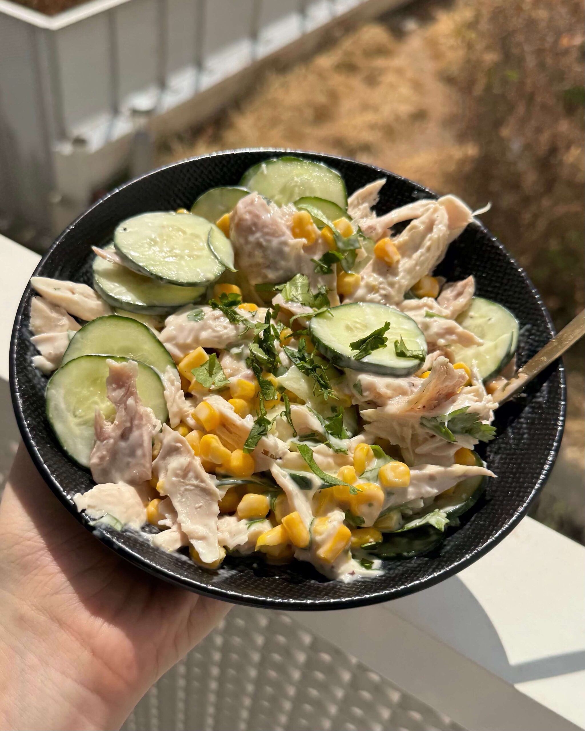 Sur un balcon ensoleillé, assiette de salade de maïs au poulet et au concombre